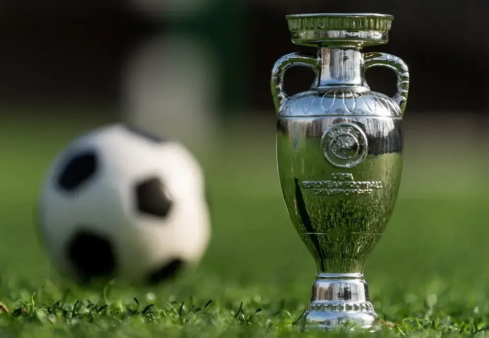 Rechts im Bild ist der Fußball EM Pokal zu sehen, links im Hintergrund ein Fußball.